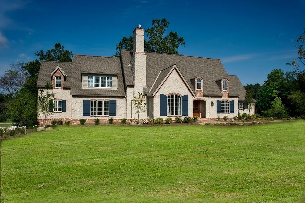 A large brick house with blue shutters is sitting on top of a lush green field.