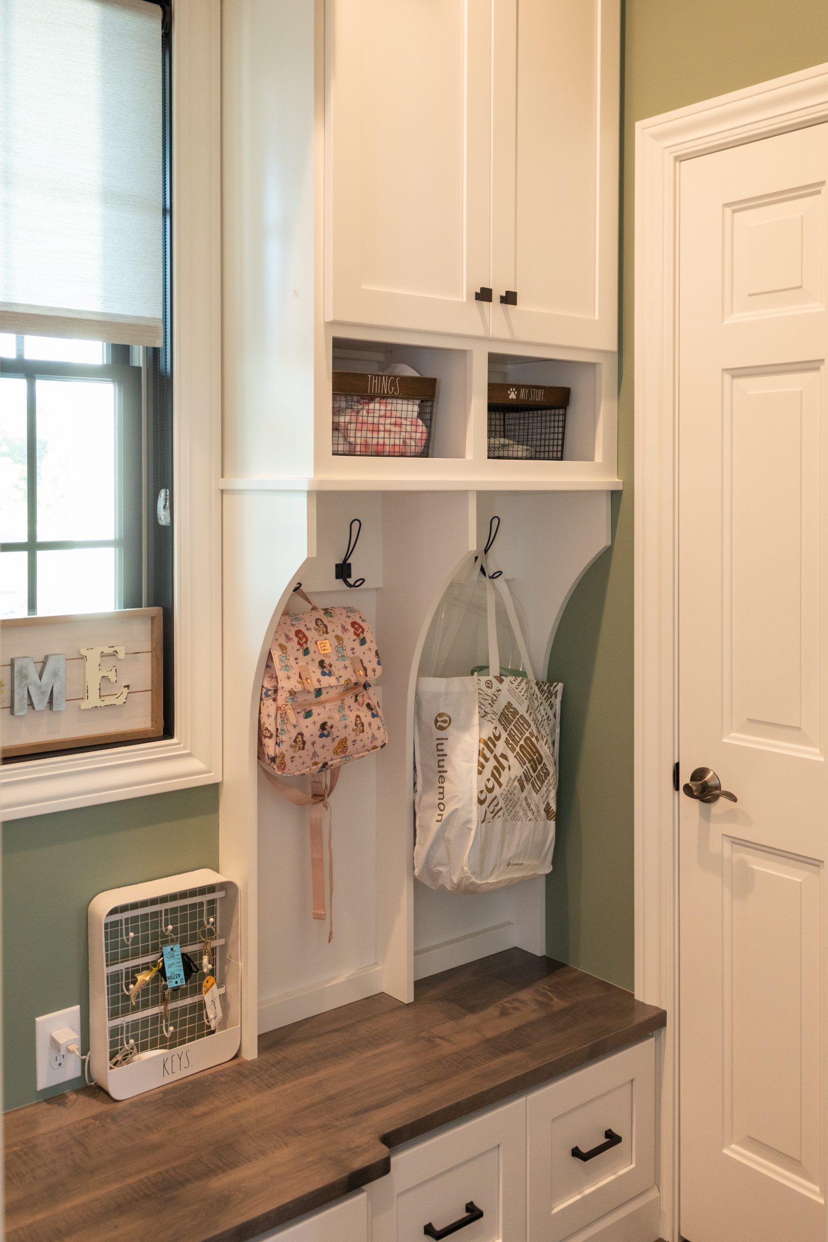 A room with white cabinets , drawers , a mirror and a bench.