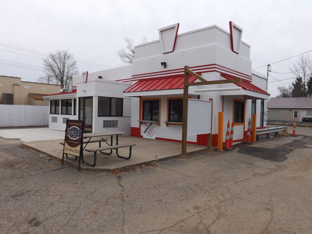 A white building with a red roof and a picnic table in front of it.