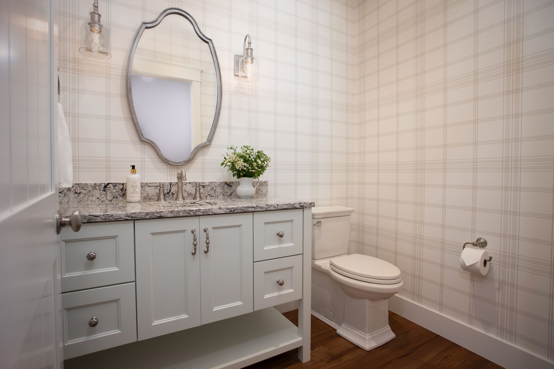 Elegant white bathroom with ornate mirror, marble vanity, and a toilet on a wood floor.