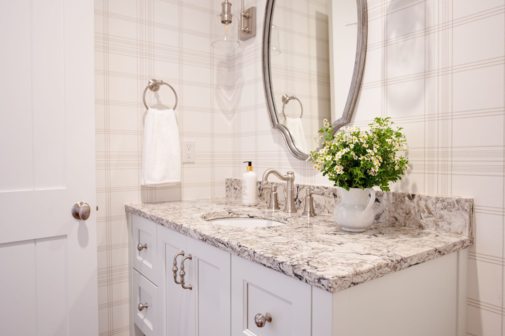 Bright bathroom vanity with granite countertop, oval mirror, white towels, and a vase of flowers.