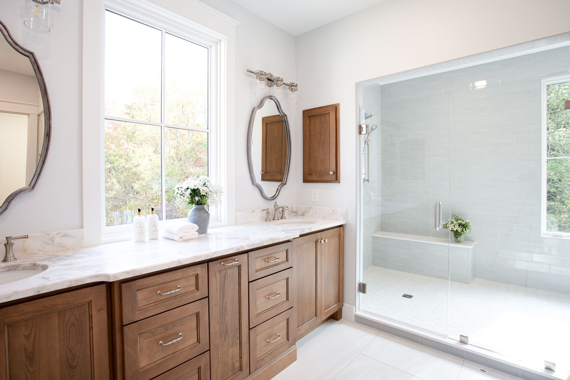 Bright bathroom with wood vanity, white countertops, and large glass shower enclosure.
