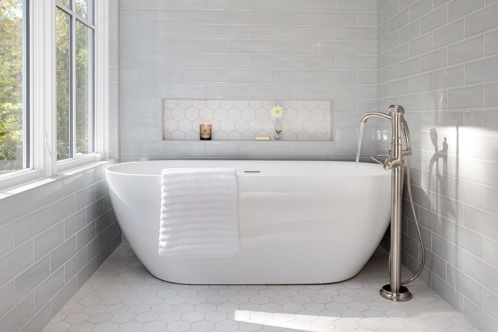 Bright white modern bathtub in a tiled bathroom with a window and chrome faucet.