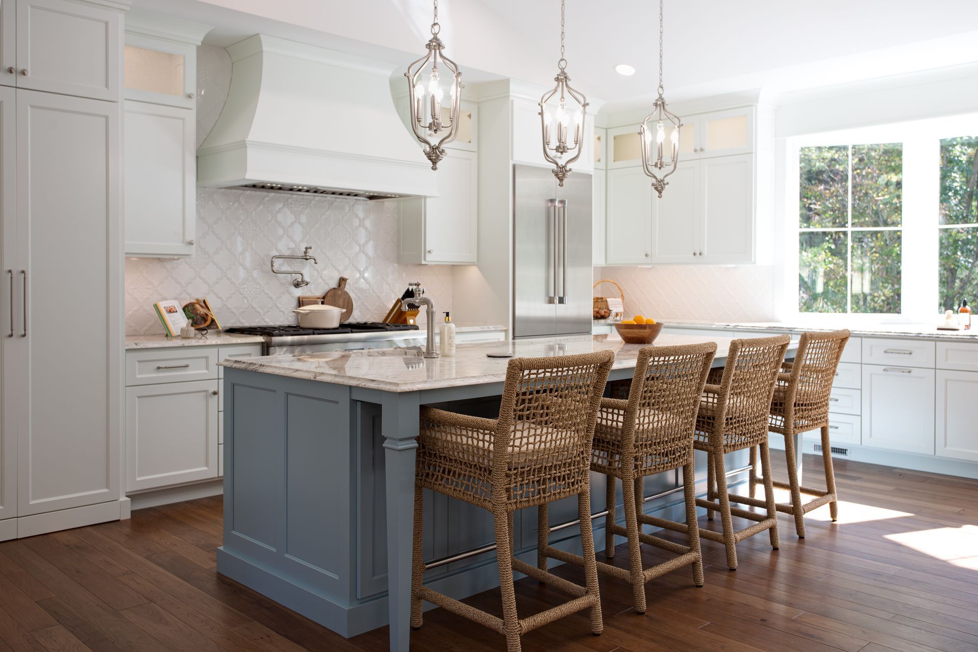 Bright modern kitchen with white cabinets, gray island, woven barstools, and pendant lights.