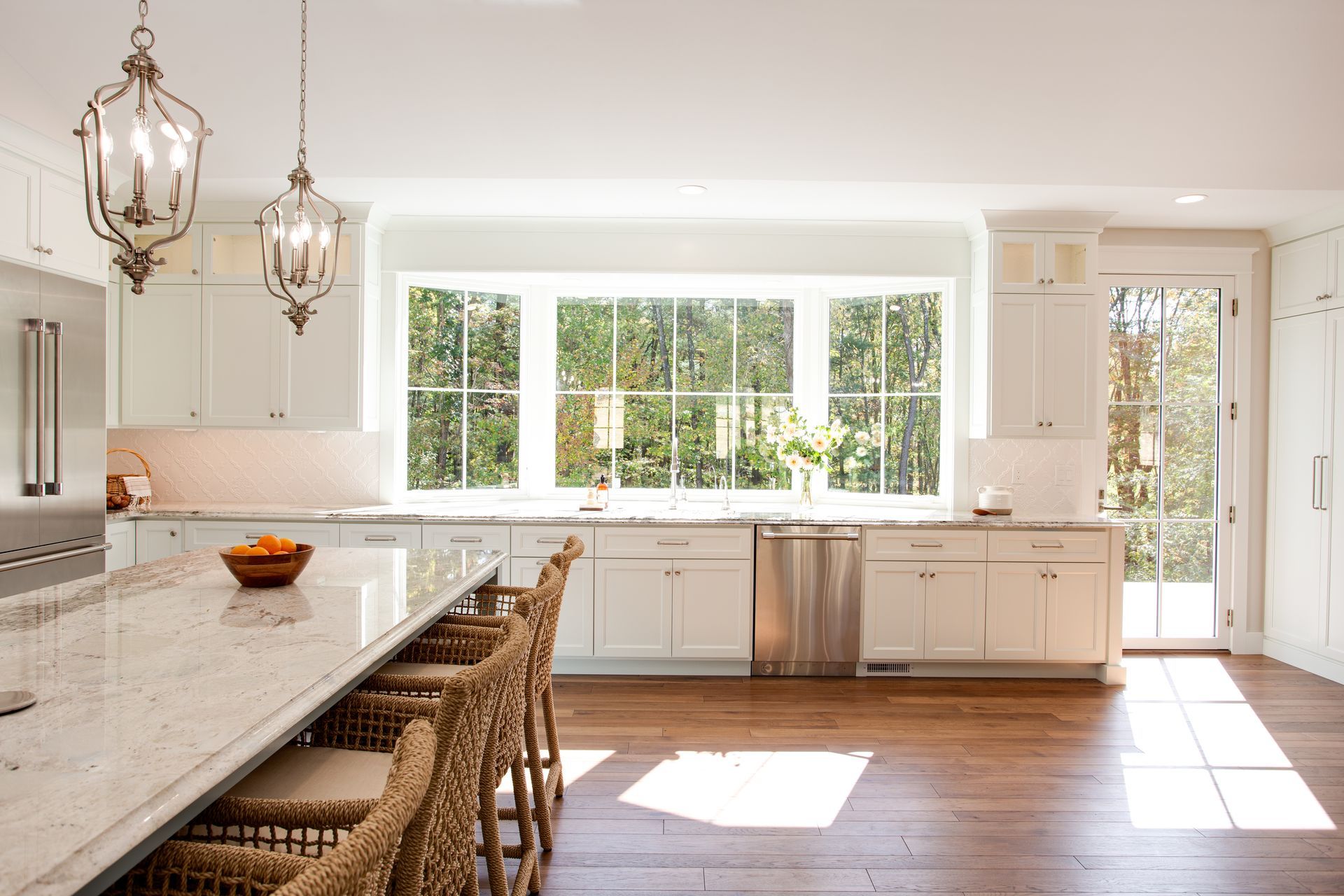 Bright modern kitchen with white cabinets, large windows, island, and wooden floor.