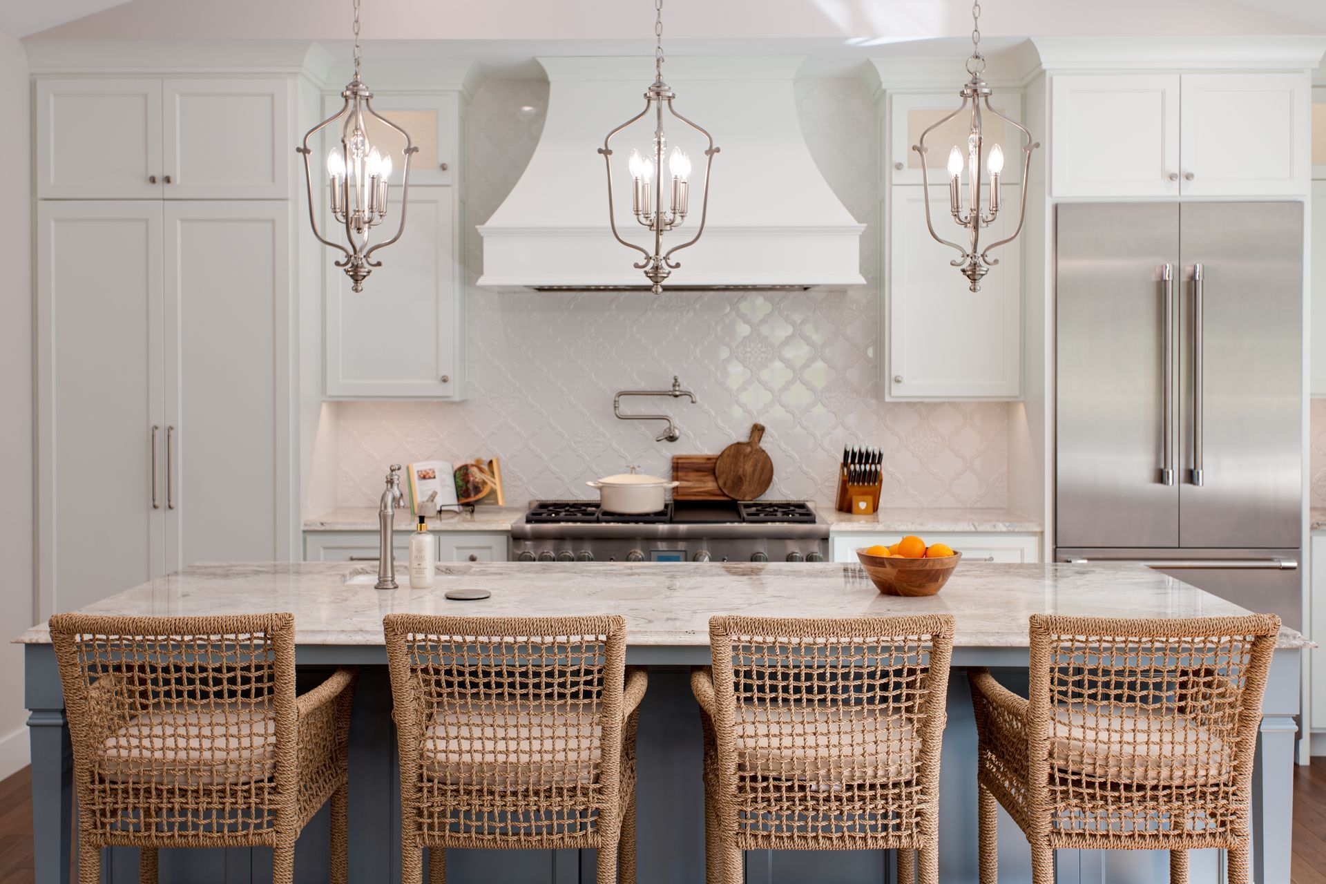 Bright white kitchen with island, wicker stools, pendant lights, and stainless steel refrigerator.