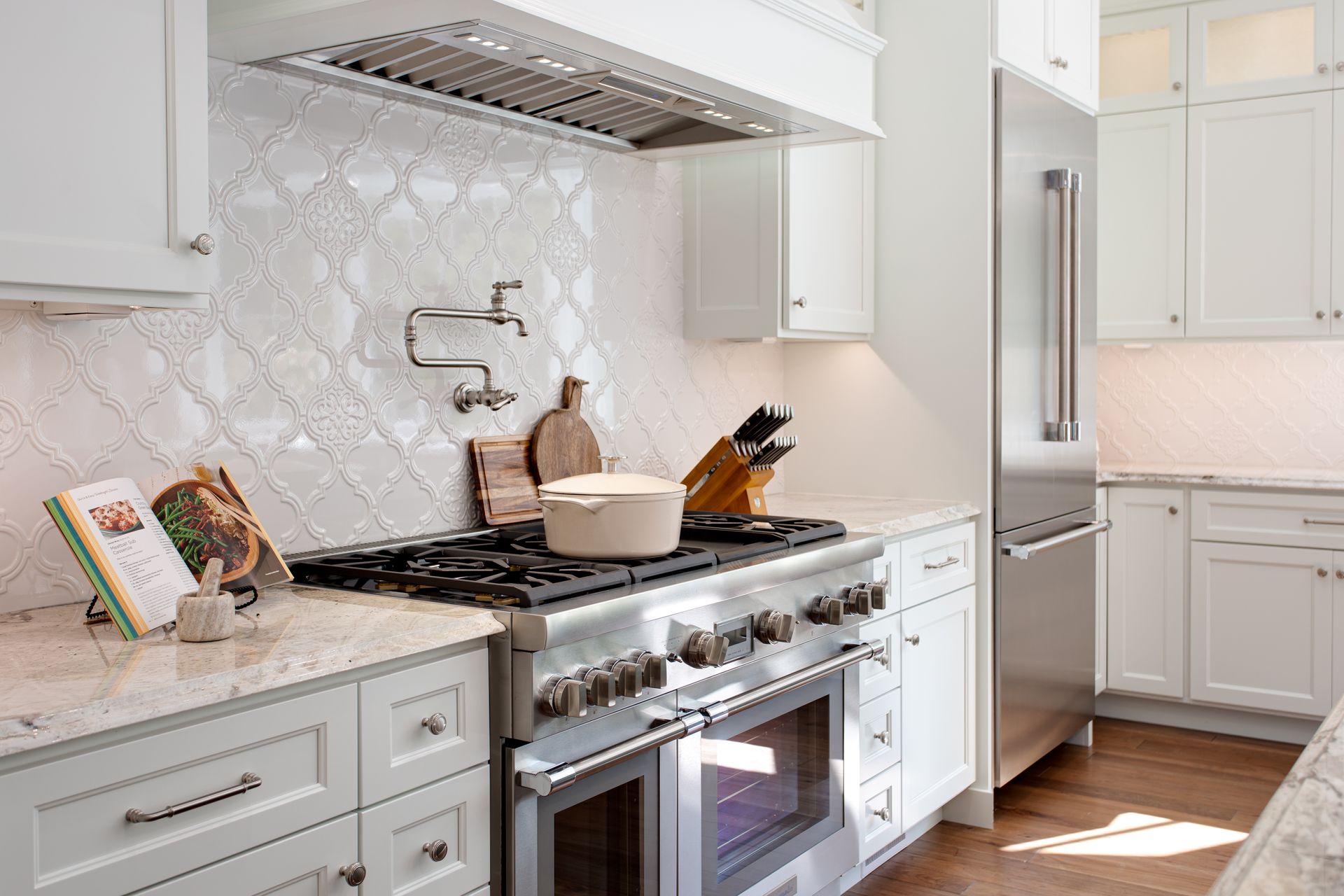 Bright white kitchen with marble backsplash, stainless range, island, and a built-in refrigerator.