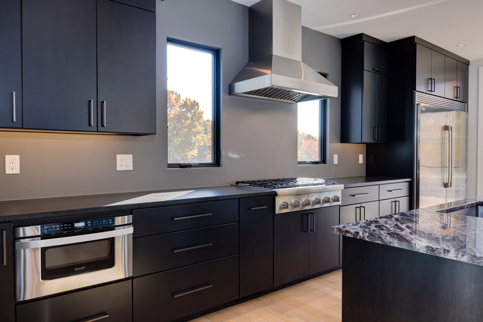 Modern kitchen with dark cabinets, stainless steel appliances, granite island, and two windows.