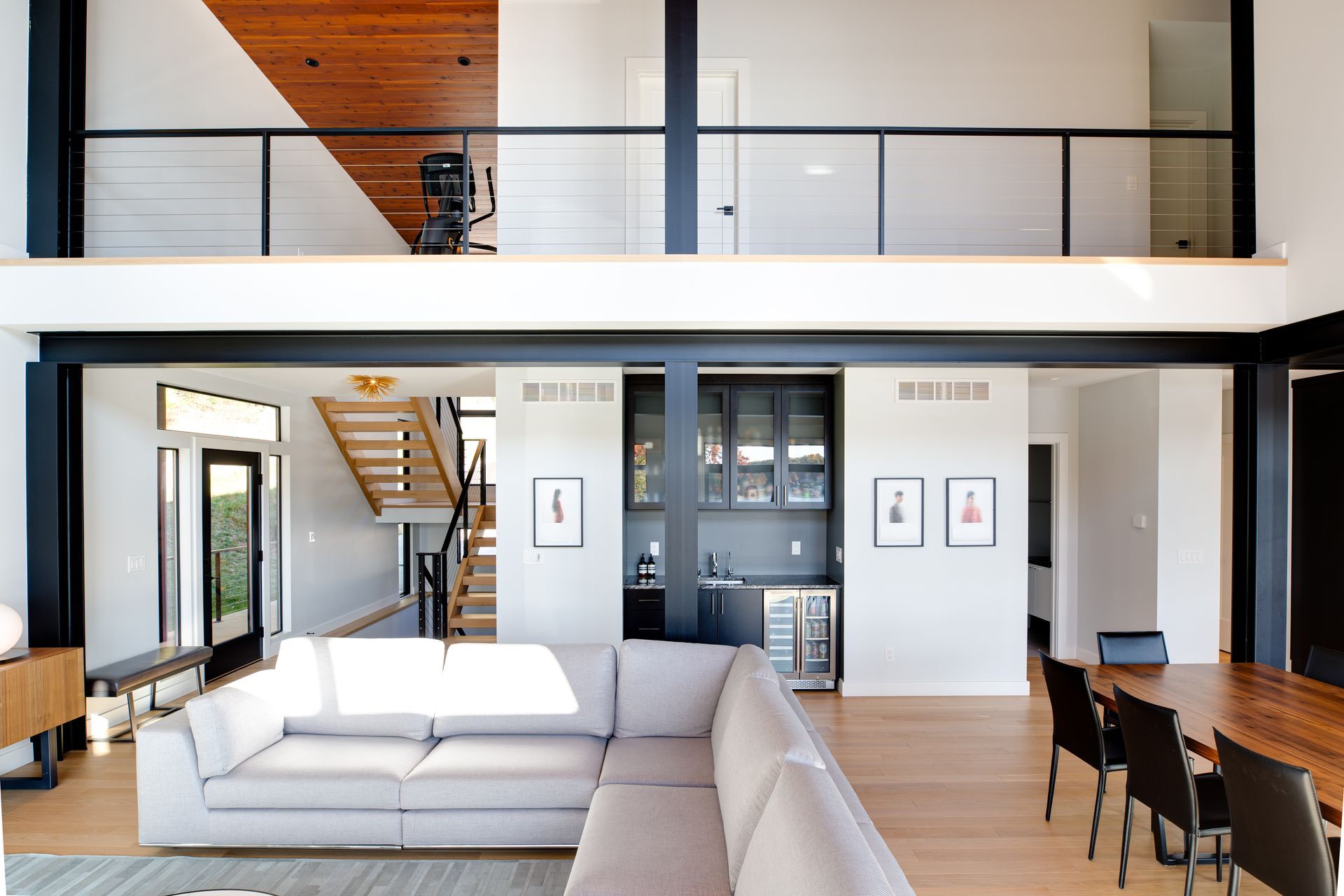 Modern open-concept living room with white sofa, wood floors, staircase, and upstairs balcony railing.