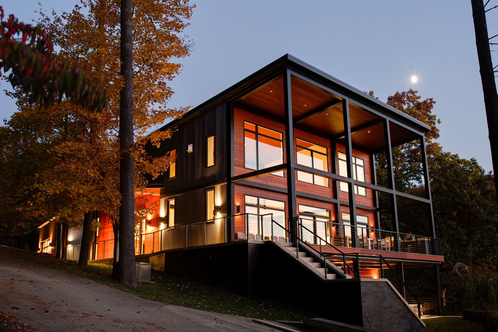 Modern style custom home at dusk with warm interior lights and autumn trees nearby.