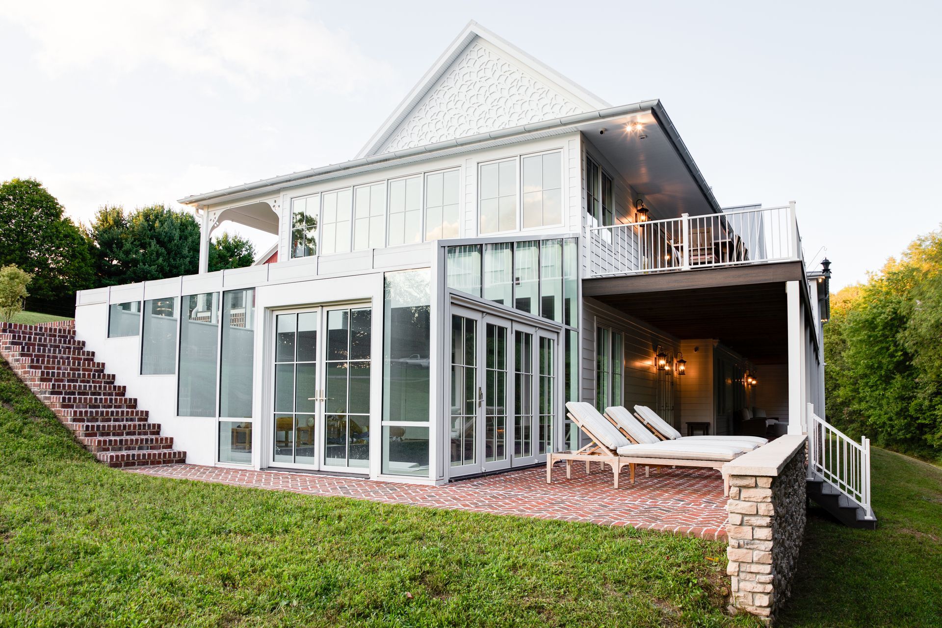White modern custom home with large glass walls, a sloped roof, and a grassy hillside foreground.