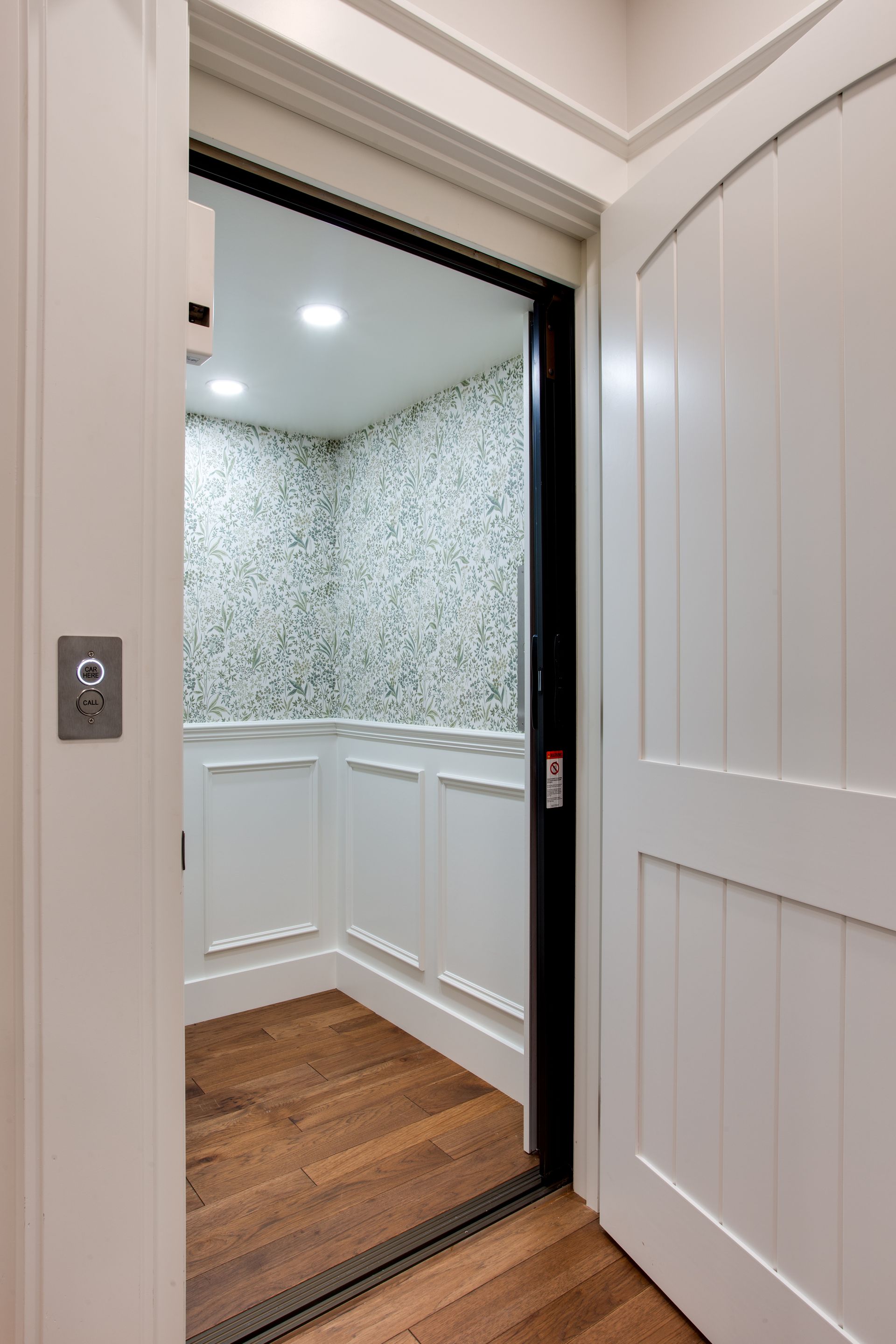 Open doorway to a small room with patterned wallpaper, white wainscoting, wood floor, and recessed lighting.