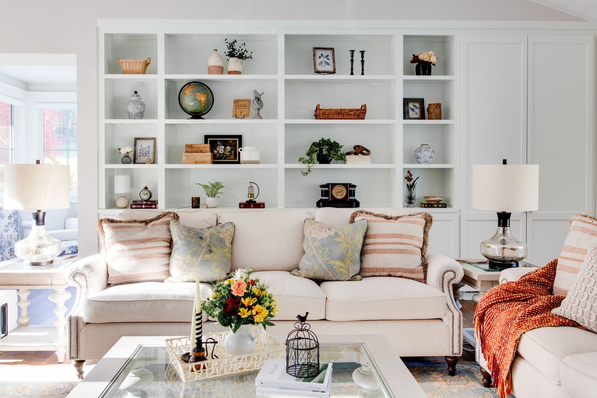 Beautiful and bright living room with white sofa, built-in shelves, coffee table, and table lamps.