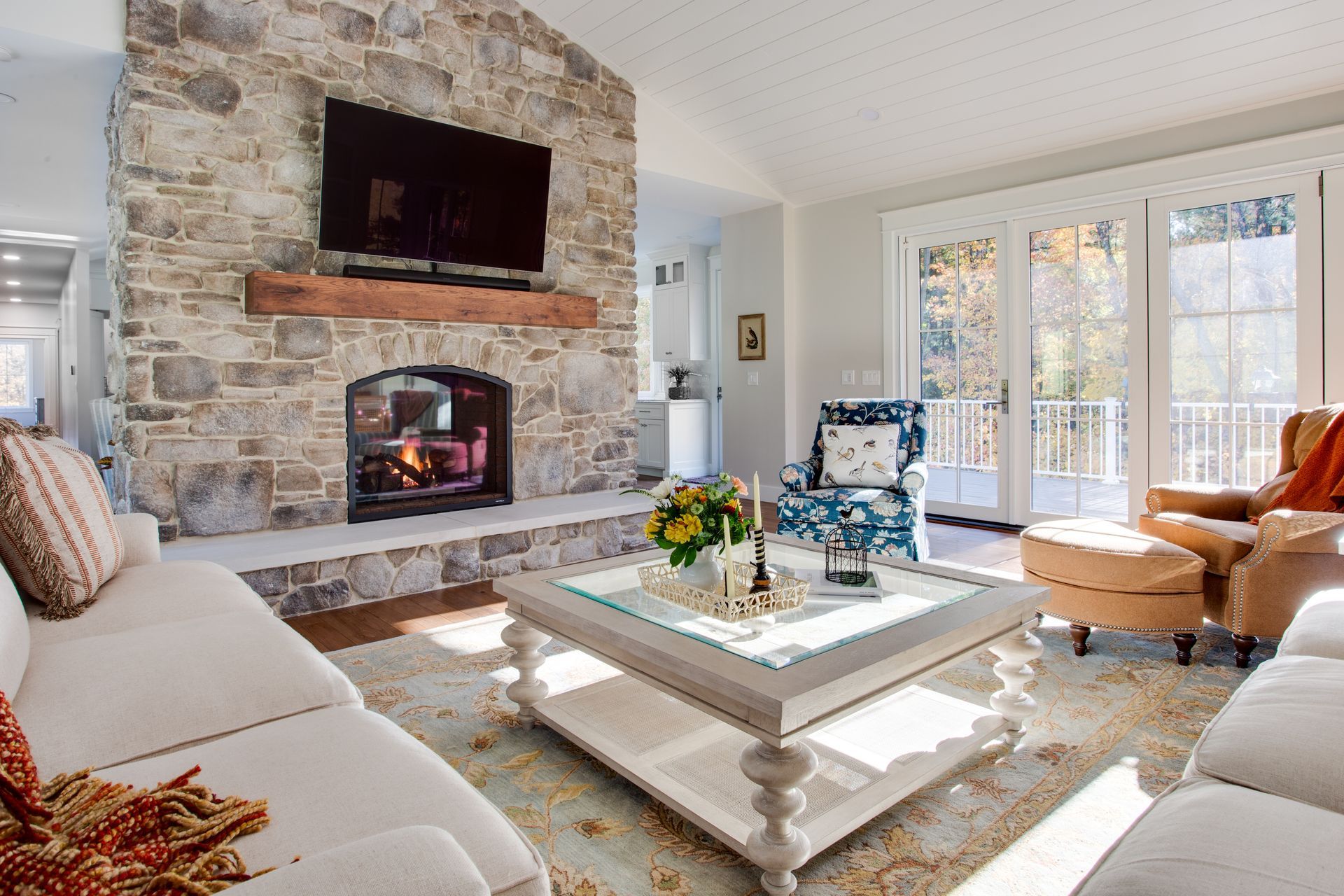 Bright living room with stone fireplace, white sofa, coffee table, and chairs by sunlit French doors.