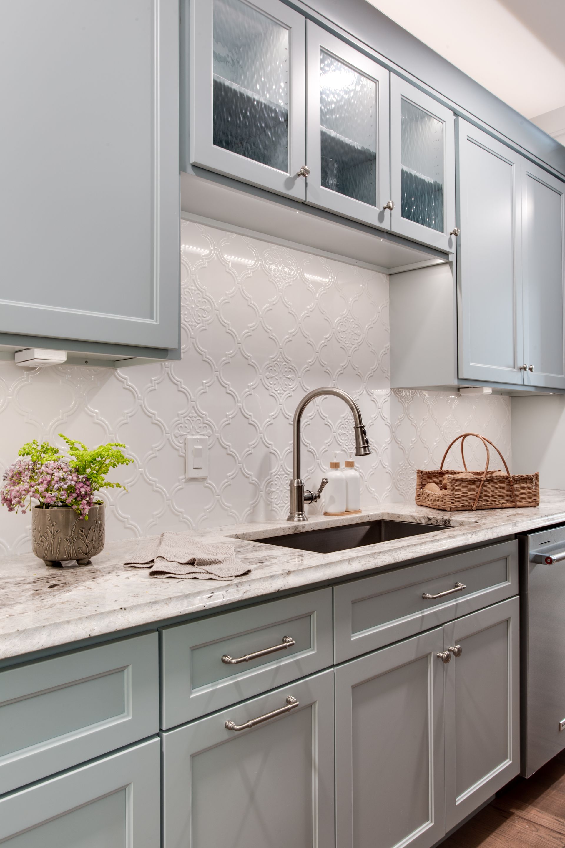 Modern white kitchen with gray cabinets, marble countertops, mosaic backsplash, and double sink.