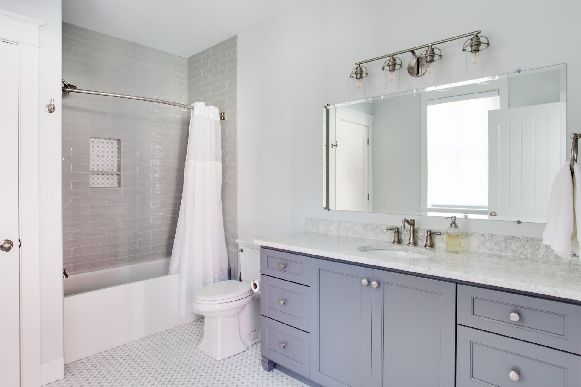 Bright modern bathroom with gray vanity, large mirror, white shower curtain, and tiled tub area.
