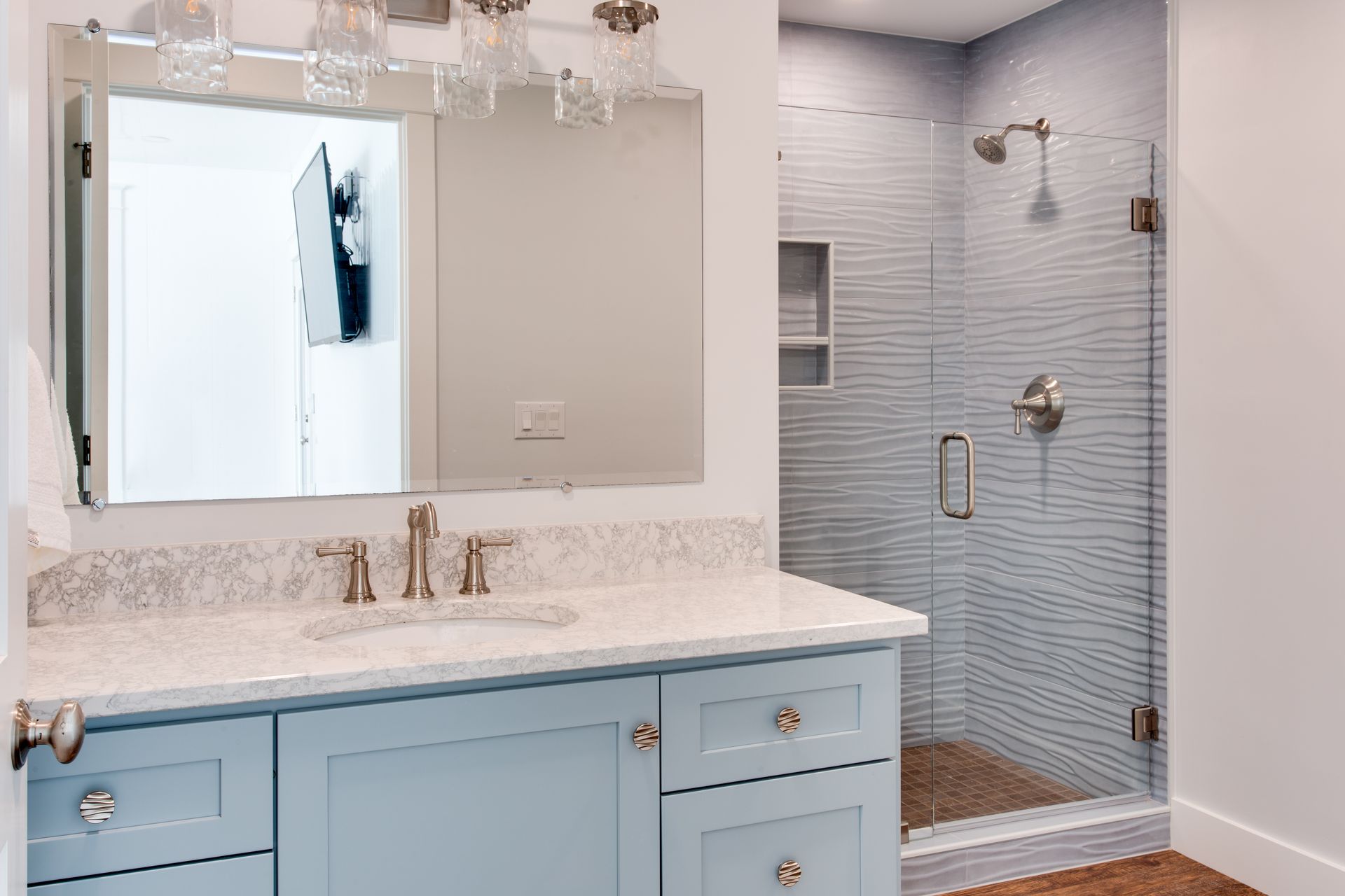Light blue bathroom vanity with mirror and adjacent tiled shower stall.
