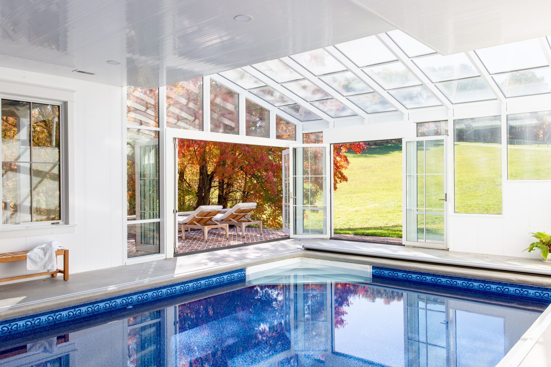 Indoor swimming pool with bright white walls, large windows, and a grassy outdoor view.