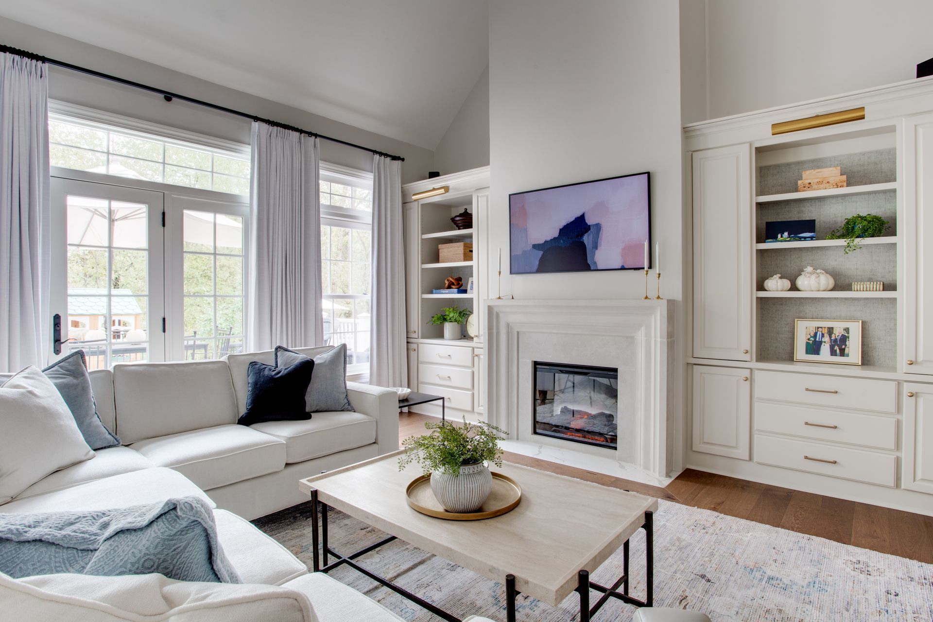Bright living room with white sofa, fireplace, built-in shelves, and large windows with curtains.