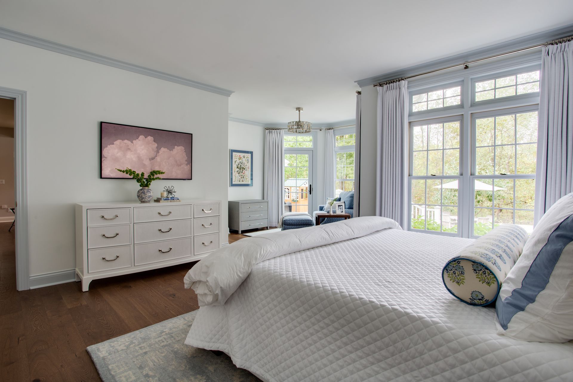 Bright bedroom with a white bed, dresser, and large windows letting in natural light.