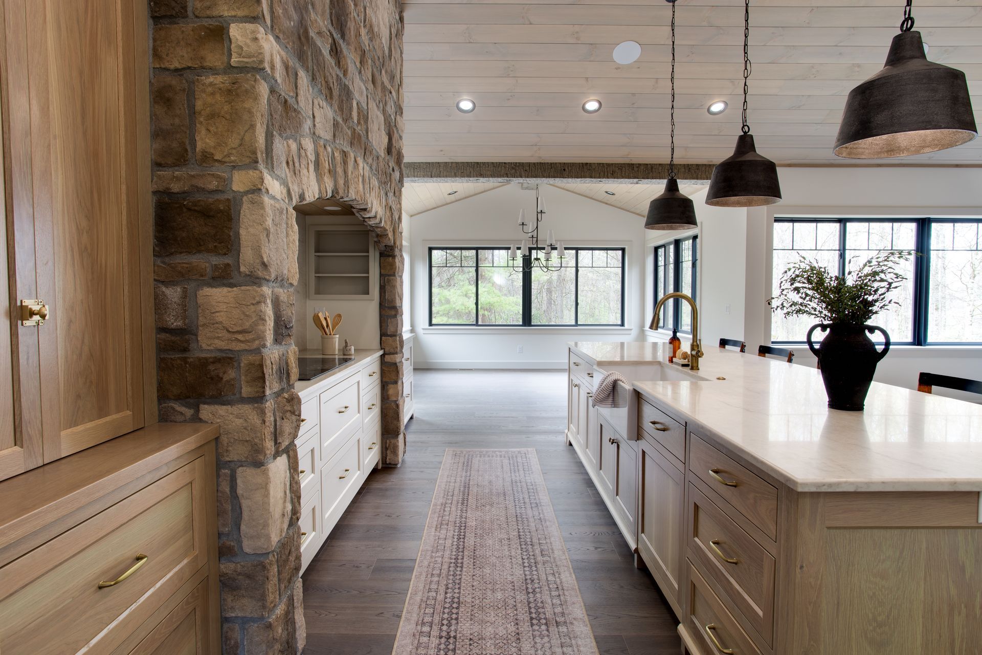 Custom modern home kitchen with stone wall, white island, pendant lights, and large windows overlooking a bright open space.