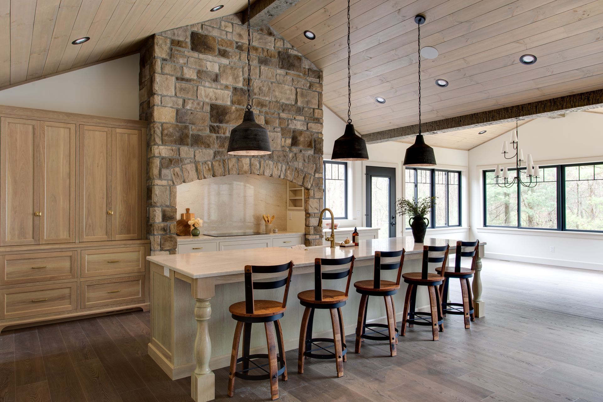 Modern kitchen with stone fireplace, wood cabinetry, island, and black pendant lights.