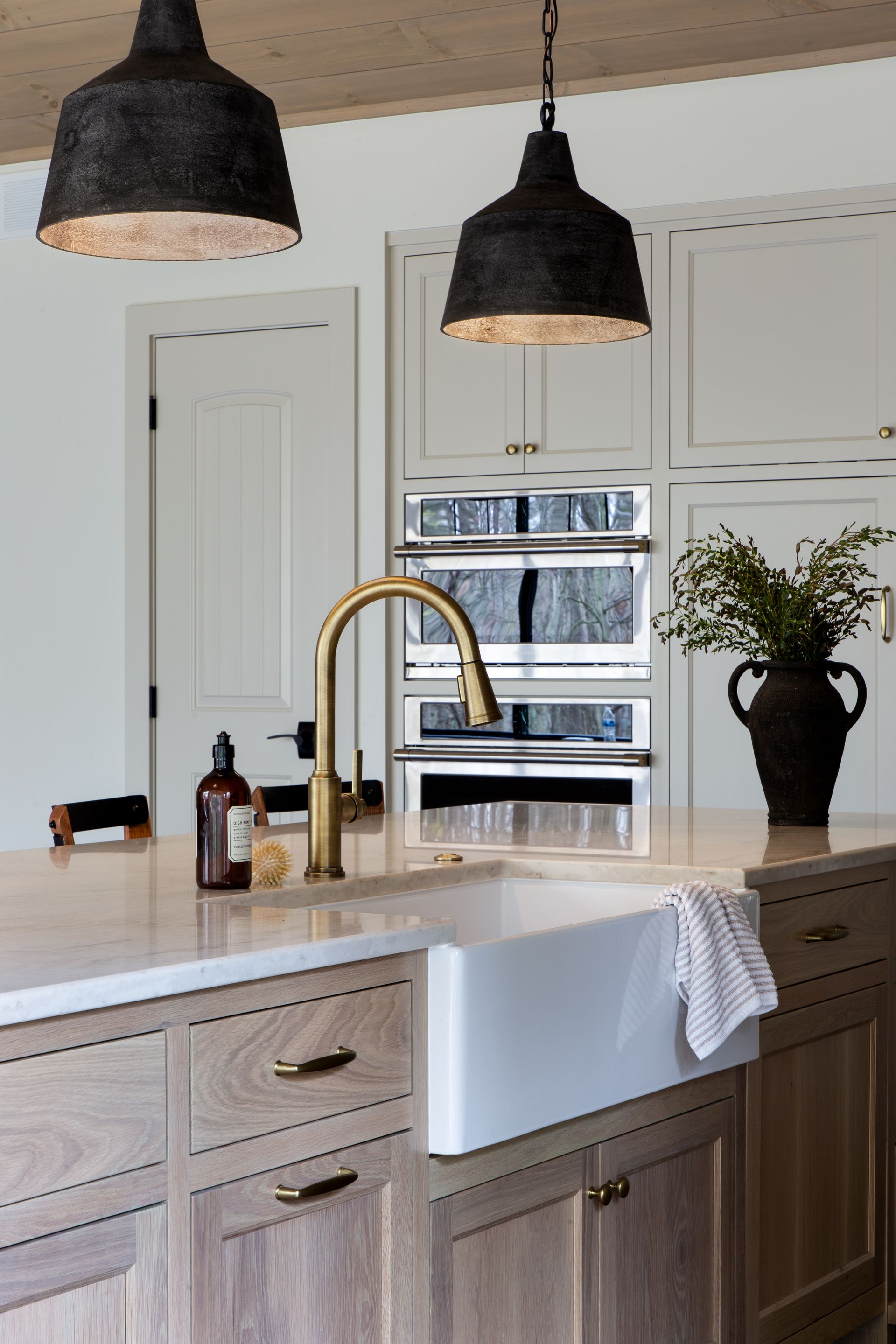 Bright kitchen with a farmhouse sink, brass faucet, pendant lights, and a vase on the island.