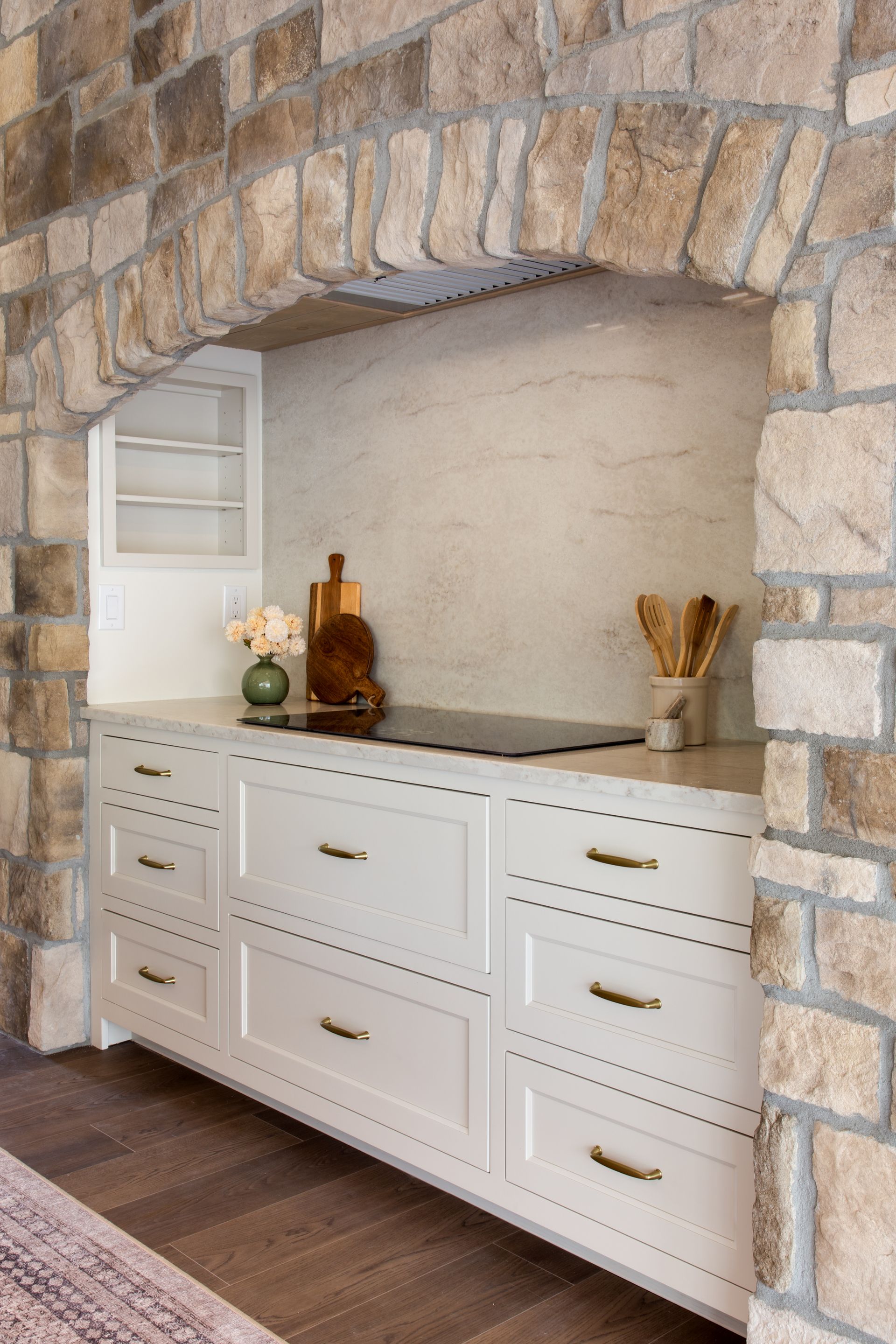 White built-in dresser with brass pulls in a stone alcove, topped with decor and a small mirror.