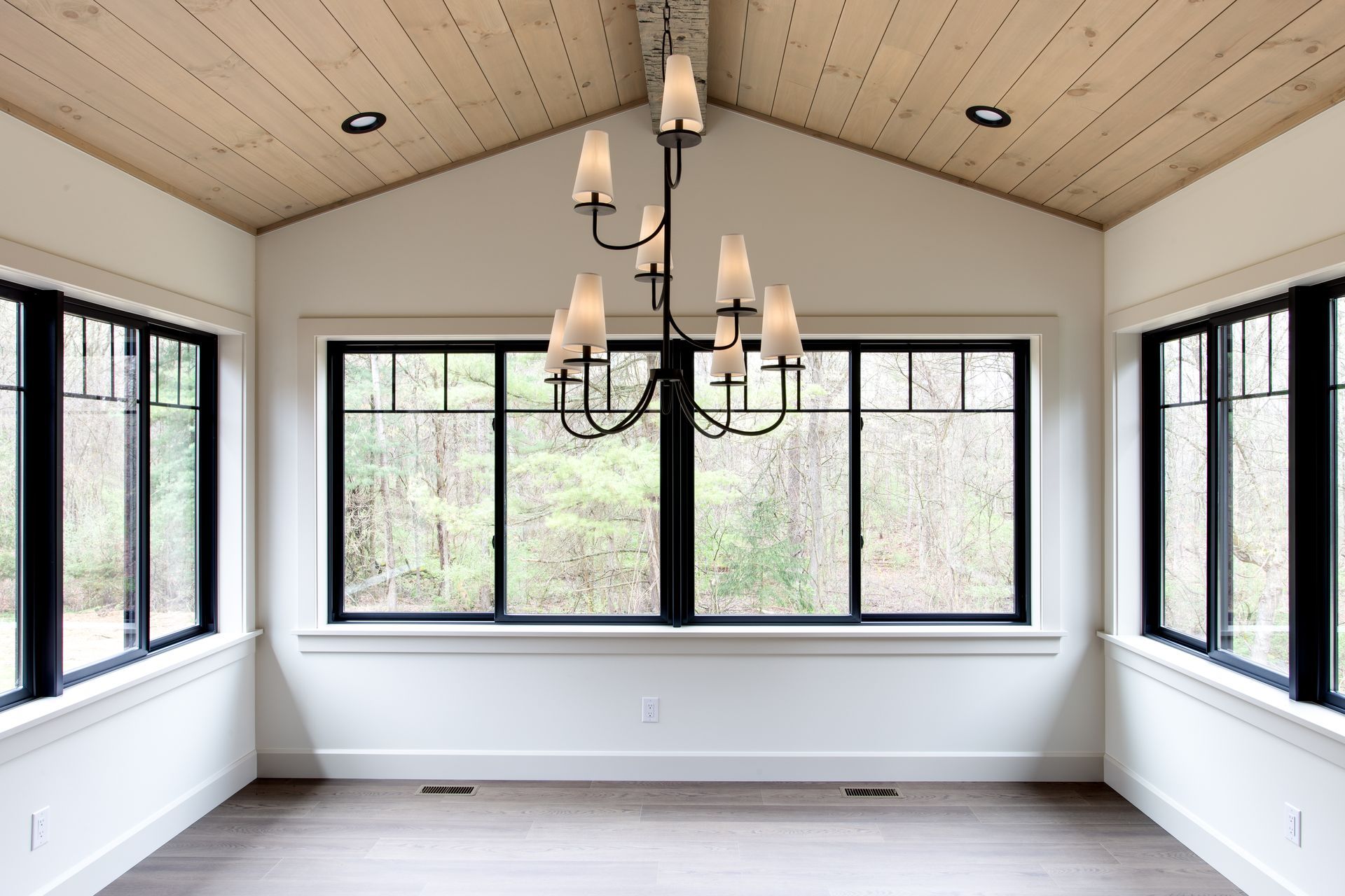 Bright room with large windows, light wood ceiling, and a black chandelier.