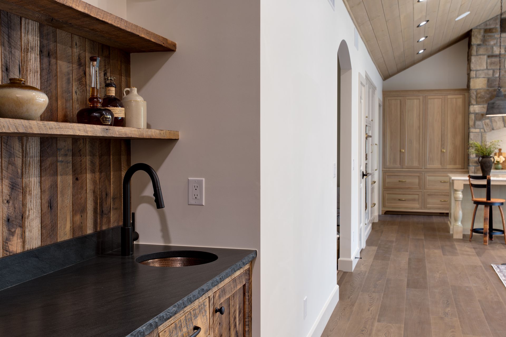 Rustic kitchen hallway with wood cabinets, black countertop, and a large pantry at the end.