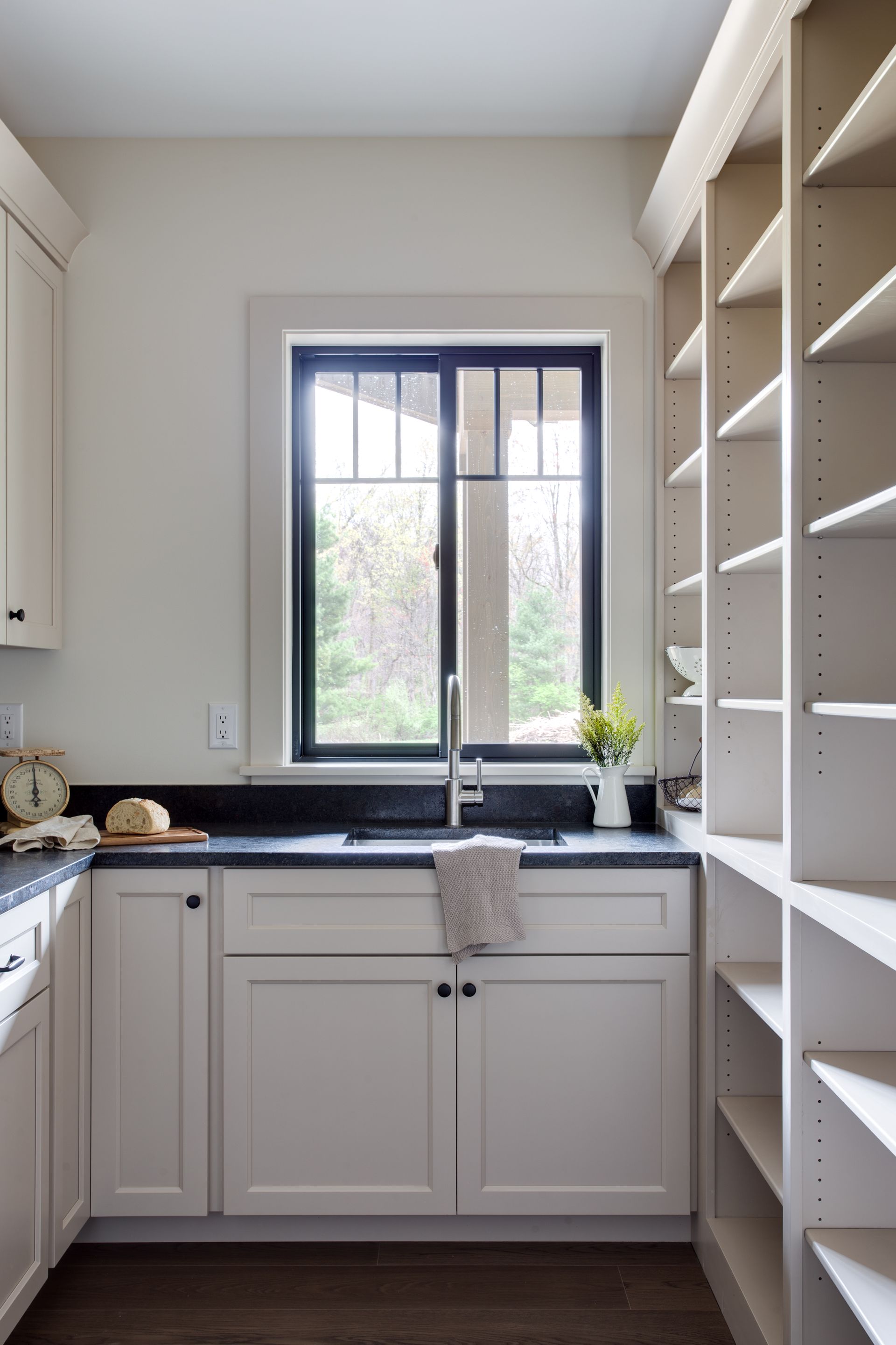 Bright kitchen with white cabinets, large window over sink, and built-in shelving on the right.
