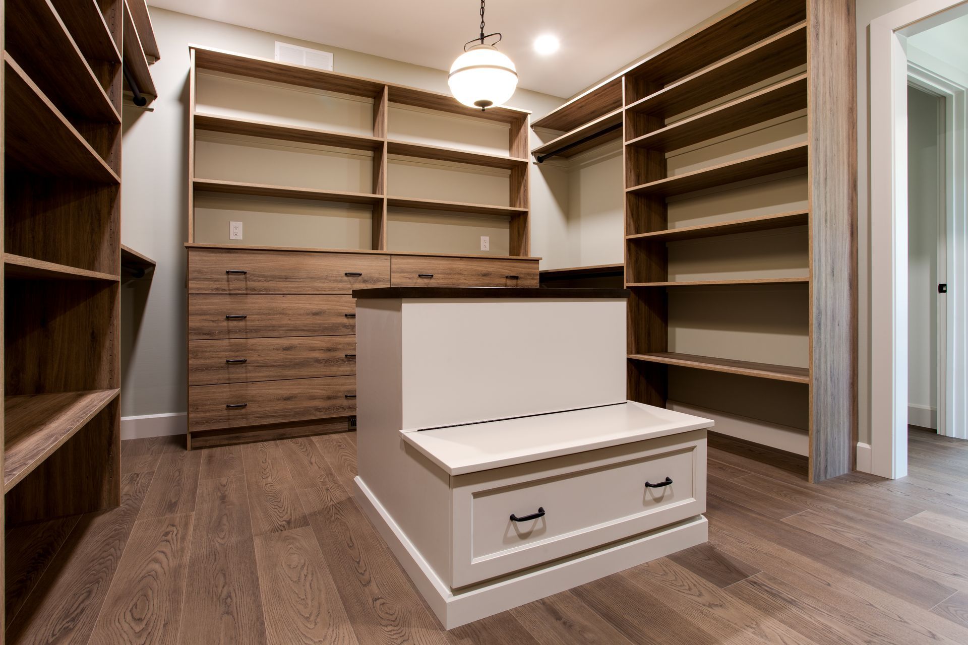 Walk-in closet of custom home with built-in wooden shelves, a central white island, and wood flooring.