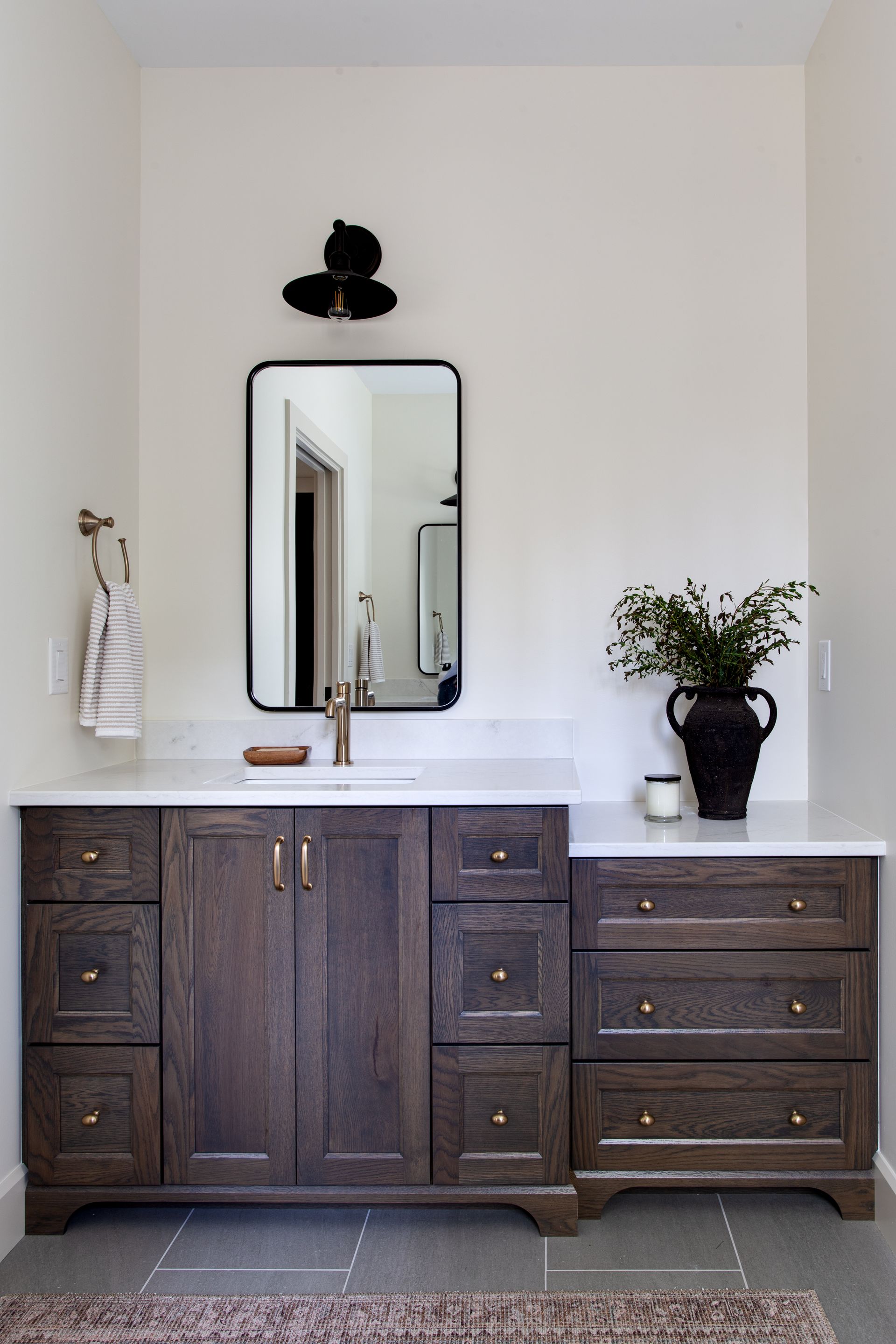 Modern bathroom vanity with dark wood cabinets, white countertop, mirror, and potted plant.