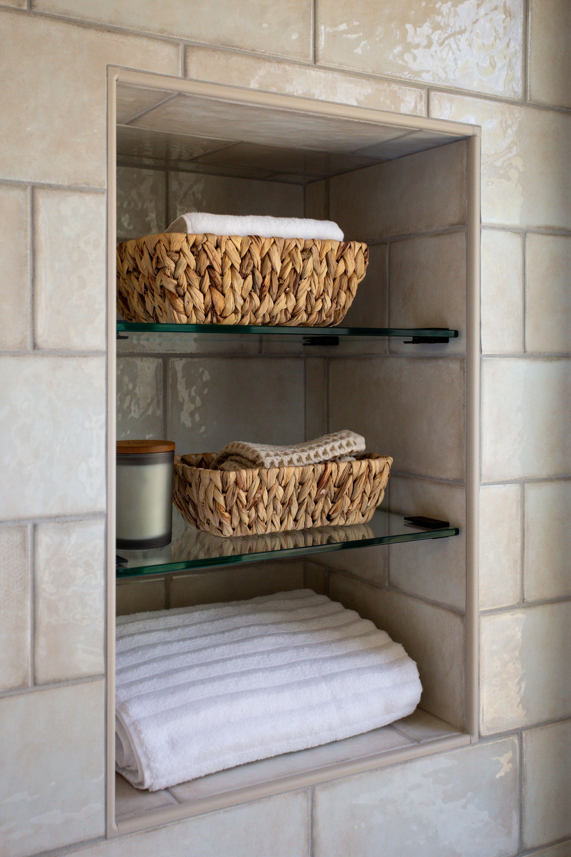 Built-in bathroom shelf with woven baskets, a candle, and folded white towels.
