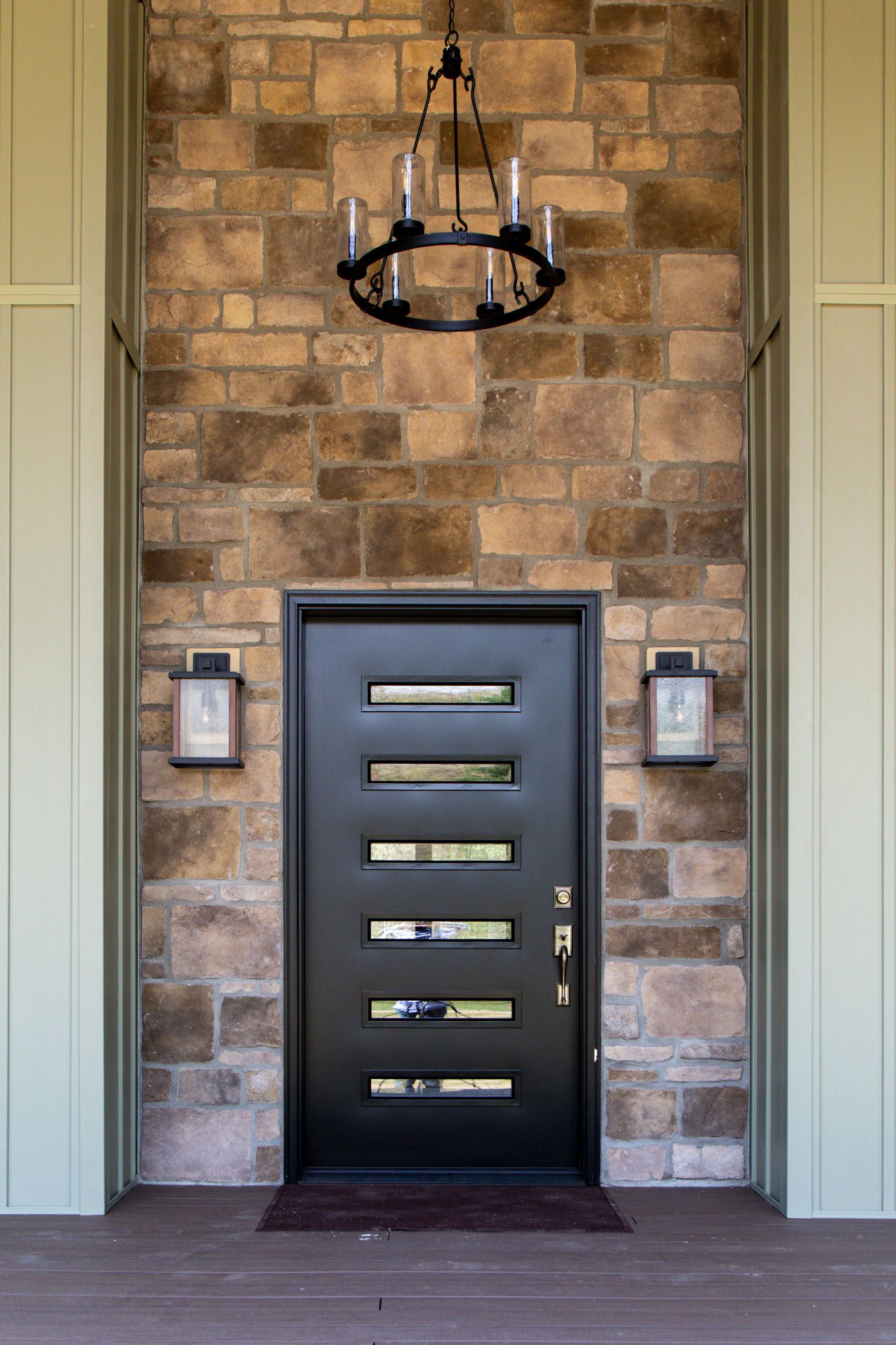 Modern front door with horizontal glass slits set in a stone facade under a hanging lantern.