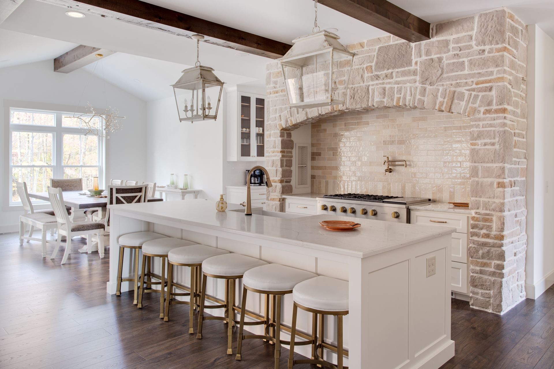 Bright white farmhouse kitchen with stone arch, island seating, and dining area by a window