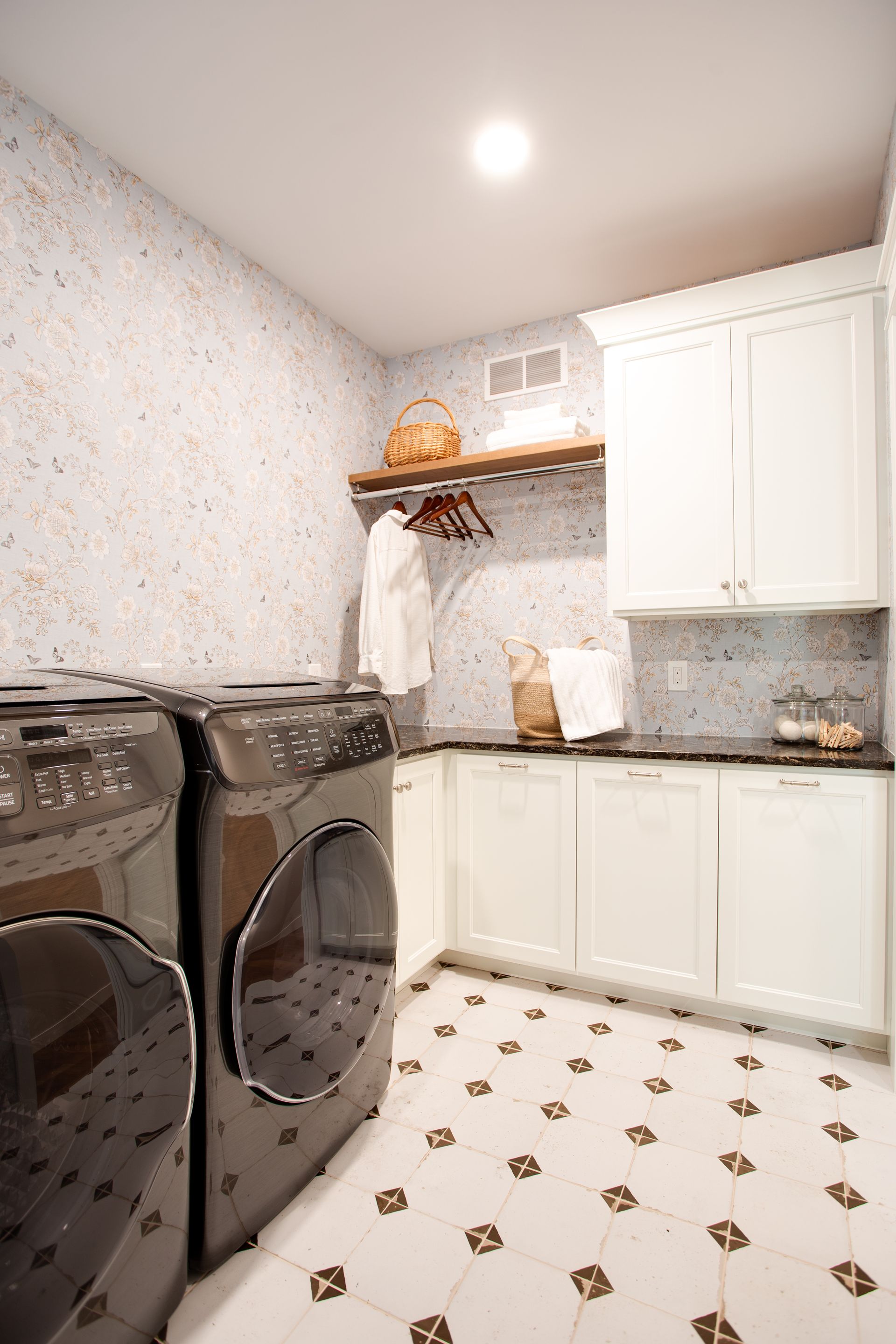 Laundry room with black washer and dryer, white cabinets, and a patterned tile floor.