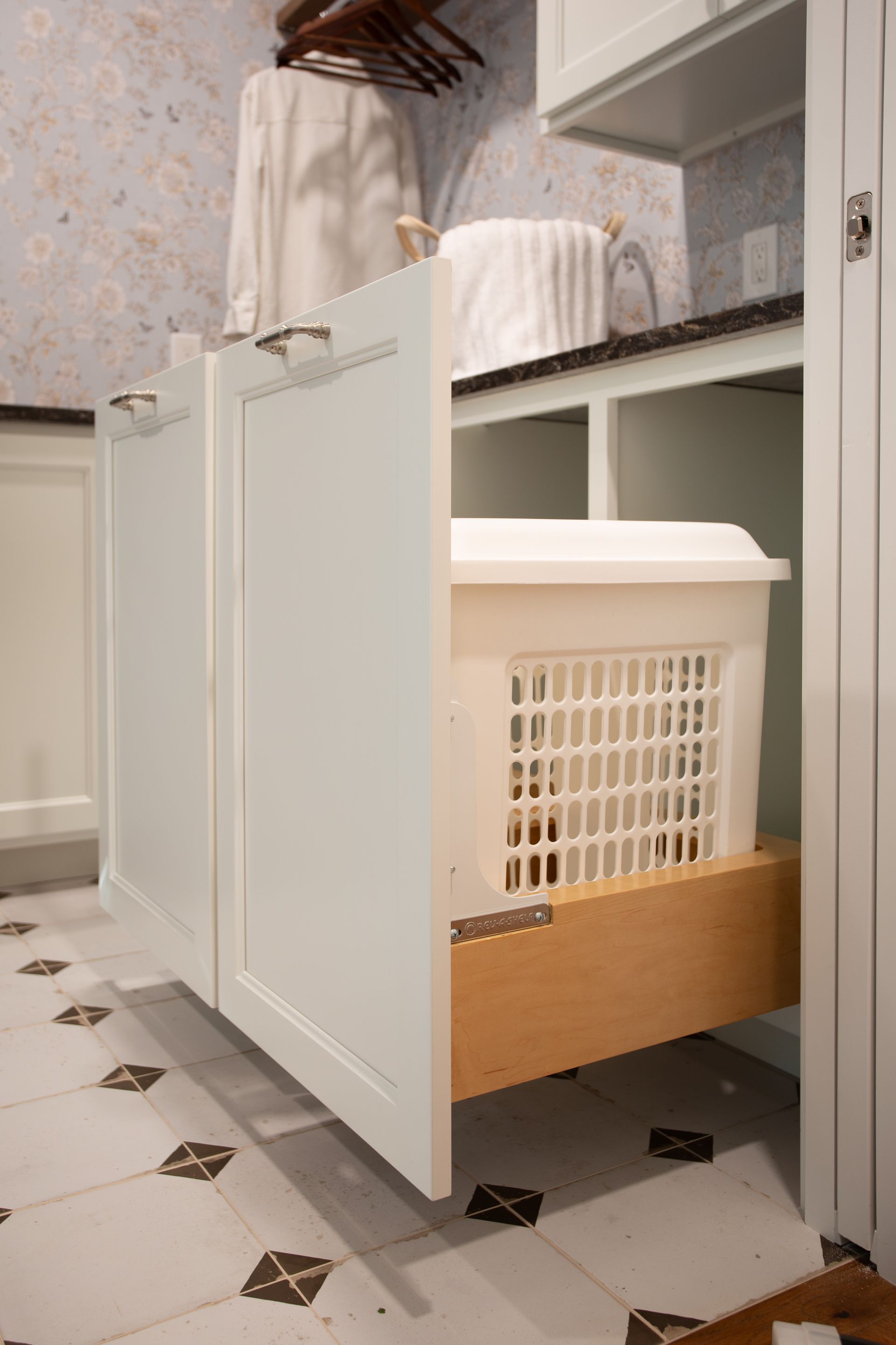 Laundry hamper in a white cabinet with open doors in a tiled room.
