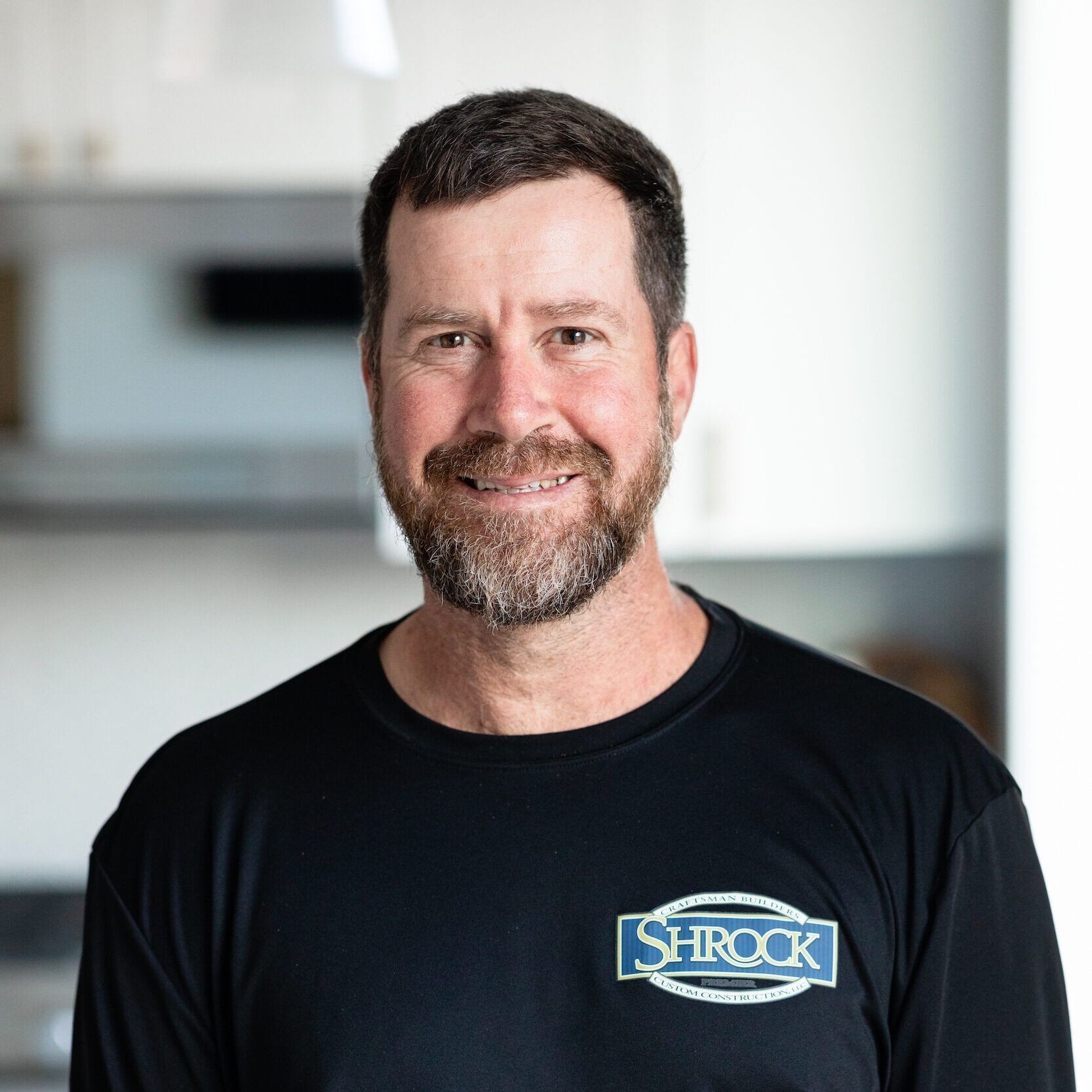 A man with a beard is wearing a black shirt and smiling for the camera.