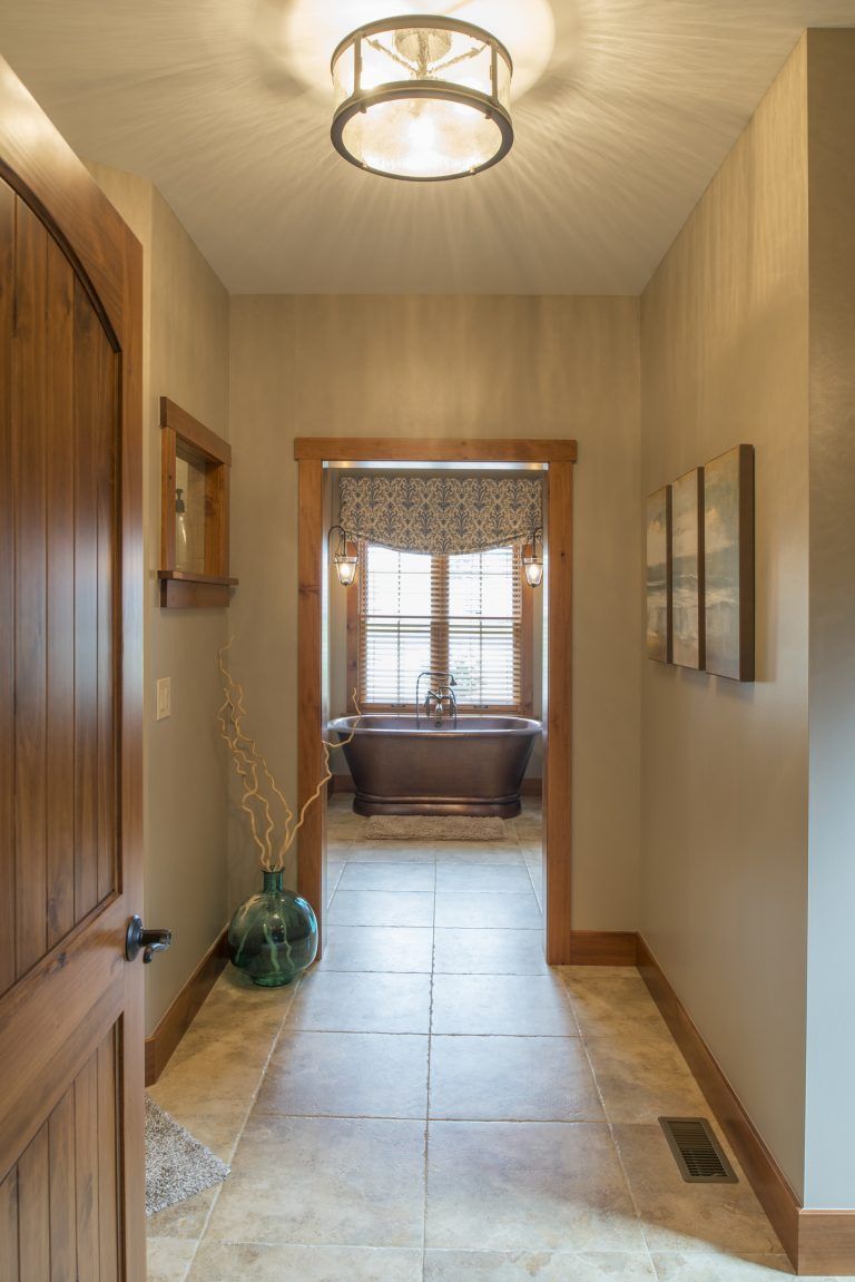 A hallway leading to a bathroom with a tub and a window.