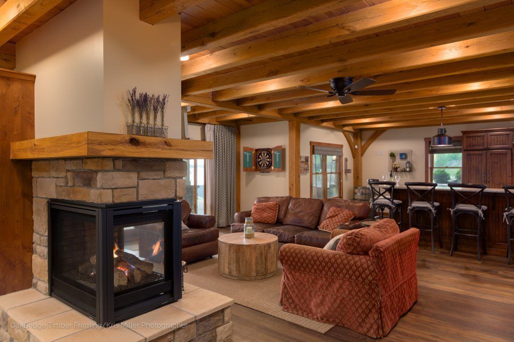 There is a fireplace in the middle of the living room with wooden ceiling.