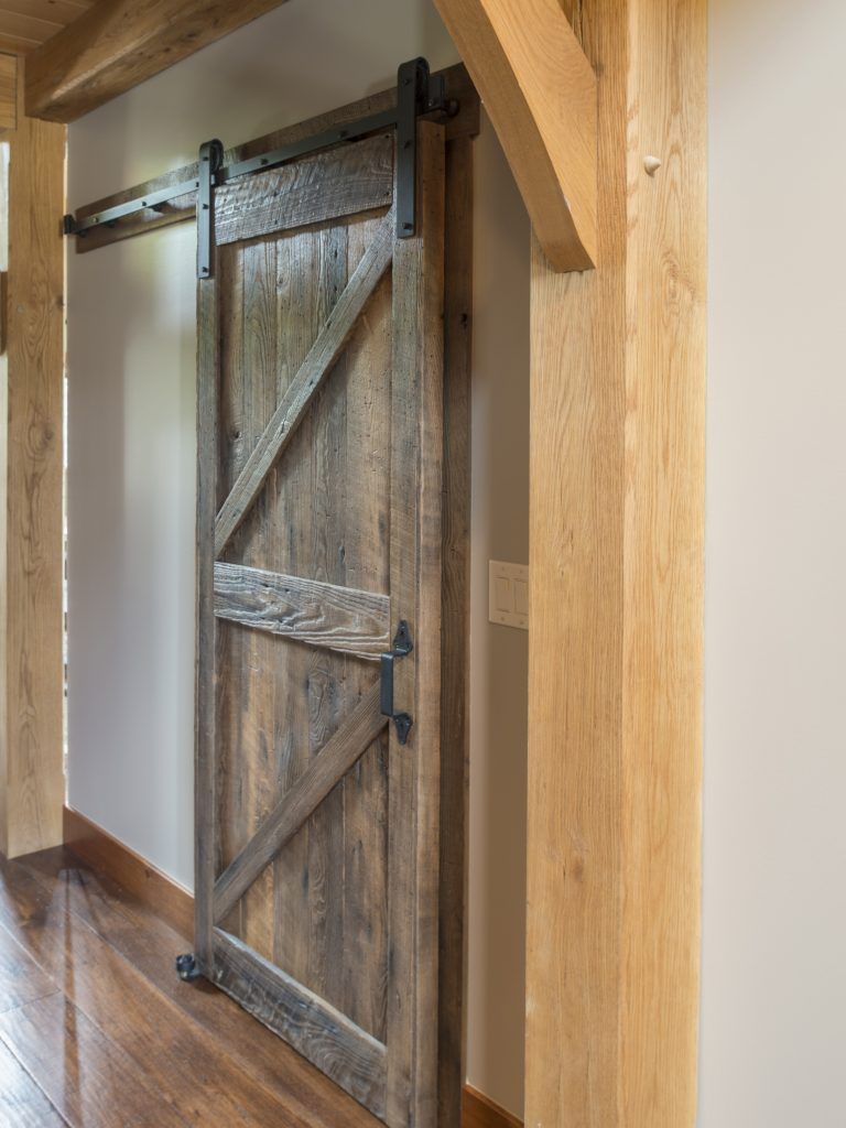 A wooden sliding barn door in a hallway with wooden beams.