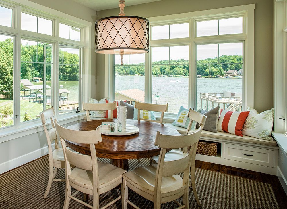 A dining room with a table and chairs and a window seat overlooking a lake.