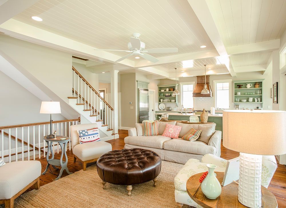 A living room with a couch, chairs, ottoman and stairs.