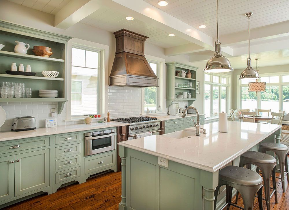 A kitchen with green cabinets, white counter tops, and a large island.