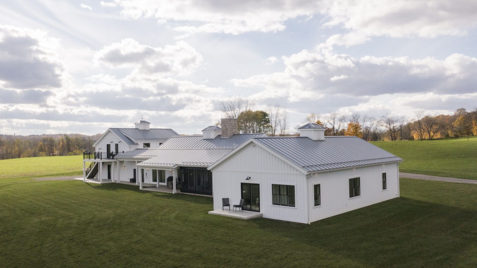 A large white house with a metal roof is sitting in the middle of a grassy field.
