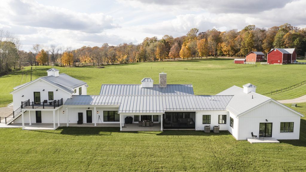 A large white house is sitting in the middle of a grassy field.