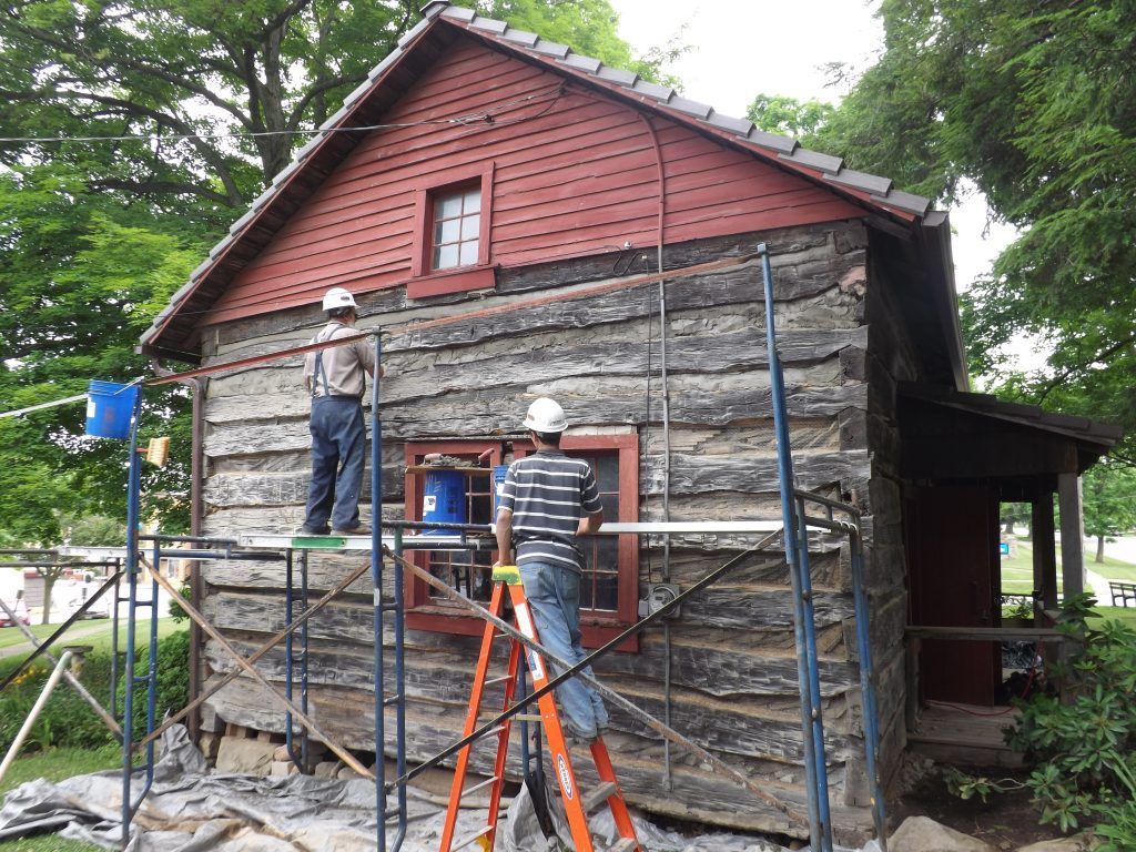 Two men are painting the side of a log cabin.