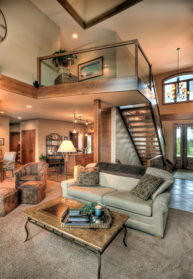 A living room with a couch, coffee table, chairs and stairs.
