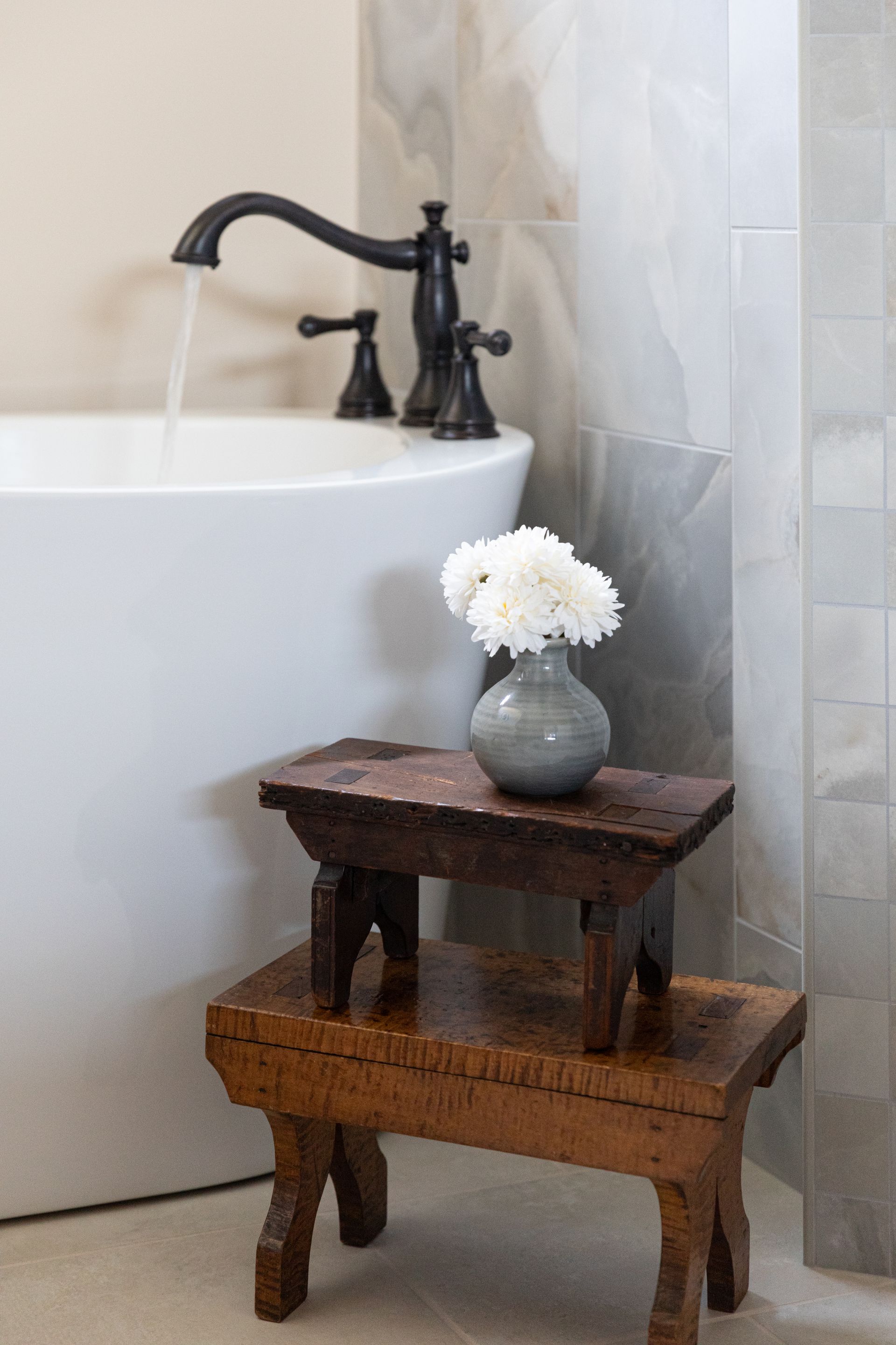 A vase of flowers is sitting on a wooden stool next to a bathtub.